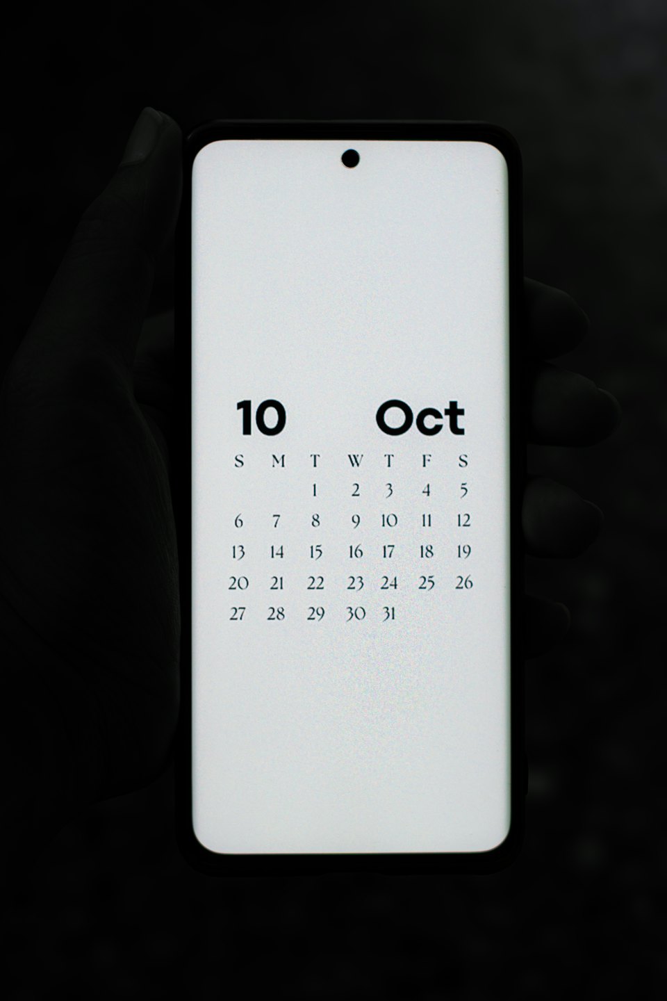 Hand holding a smartphone showing an October calendar screen.